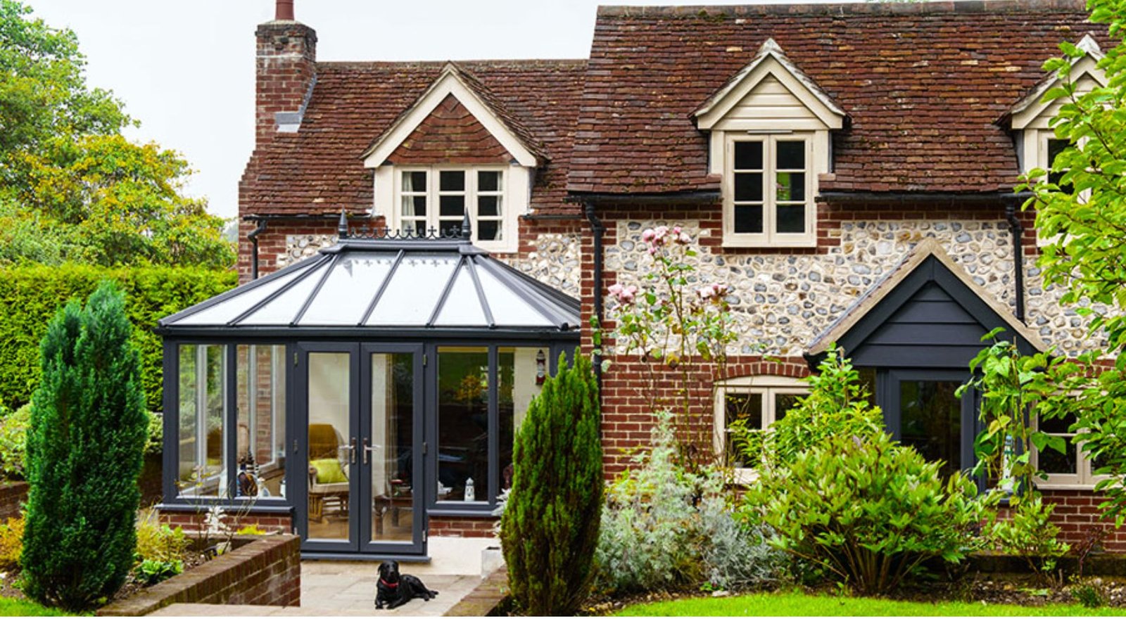 A home with a glass-roofed conservatory surrounded by a vibrant garden, blending indoor and outdoor living.
