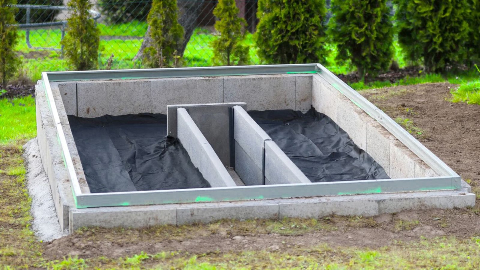 Soil and grass surrounding a greenhouse foundation, highlighting an area ready for gardening activities.
